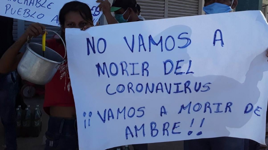 Una mujer sostiene con una mano un balde metálico y con la otra un cartel escrito a mano que dice «No vamos a morir del coronavirus, ¡¡vamos a morir de ambre!!». Detrás hay otras personas con barbijo y más carteles.